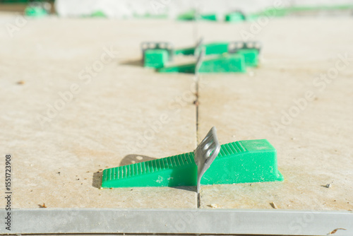 Green plastic clips and wedges for tile leveling on a fresh floor, concept of construction, renovation, finishing