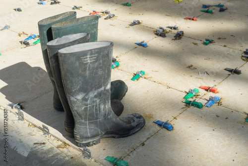Pair of tall black rubber boots on newly laid tiles with clips and wedges, concept of construction, renovation, tilling