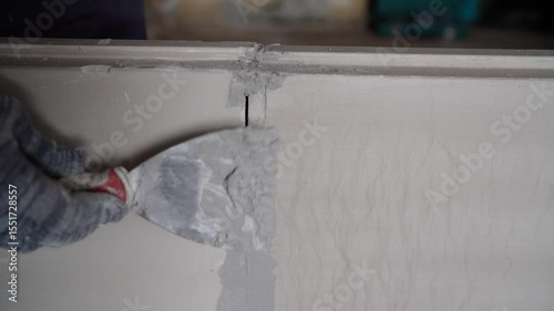 Construction worker carefully repairing wall crack using putty knife, smoothing surface with professional skill during home improvement project