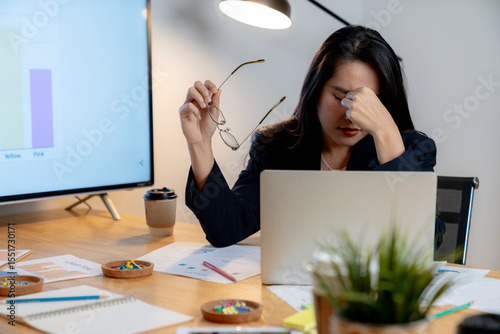 Exhausted female office worker feeling eye fatigue after working late hours in front of a computer.