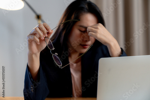 Exhausted female office worker feeling eye fatigue after working late hours in front of a computer.