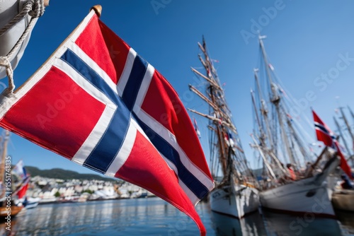 Norwegian flag waving near historic ships in harbor during bright sunny day with clear blue skies photo