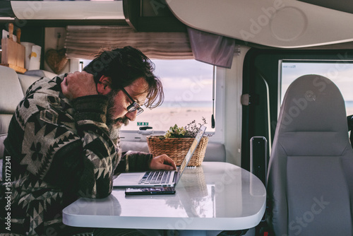 Mature man working remotely from inside a camper van, focused on his laptop while enjoying the freedom of travel. Digital nomad lifestyle, technology on the road, independence and modern remote work