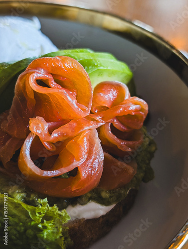 Vertical image of a healthy toast with smoked salmon, poached egg, avocado, and green salad on a plate in a cafe