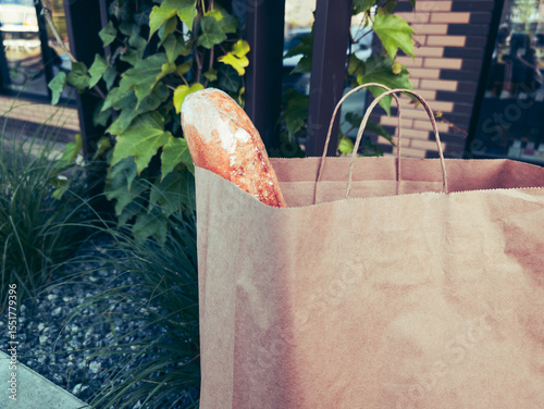 craft paper bag with fresh baguette inside, placed on the sidewalk