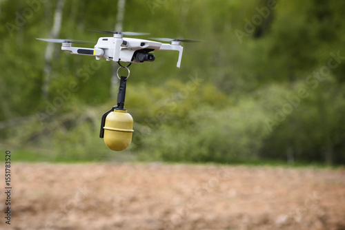 Small Flying unmanned aerial vehicle in flight mode with camera with a grenade attached sideways outdoor green forest plowed field