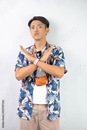 Young asian man wearing blue summer shirt is showing rejection hand gesture, isolated over white background