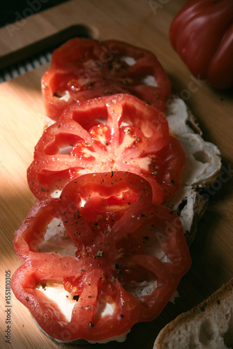 A rustic flat lay featuring slices of homemade artisan bread, fresh heirloom tomato, peppers on a wooden kitchen table. Natural light and cozy farmhouse aesthetics