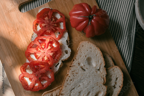 A rustic flat lay featuring slices of homemade artisan bread, fresh heirloom tomato, peppers on a wooden kitchen table. Natural light and cozy farmhouse aesthetics