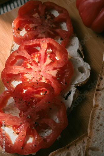 A rustic flat lay featuring slices of homemade artisan bread, fresh heirloom tomato, peppers on a wooden kitchen table. Natural light and cozy farmhouse aesthetics