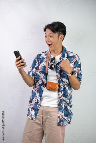 Happy young asian man wearing blue summer shirt is holding a smartphone with blank screen for mock up mockup, isolated over white background.