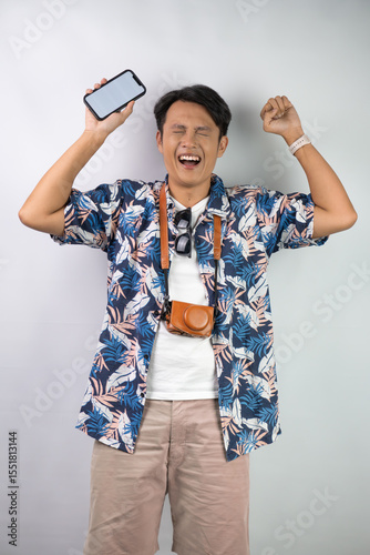 Happy young asian man wearing blue summer shirt is holding a smartphone with blank screen for mock up mockup, isolated over white background.