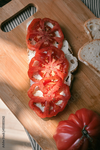 A rustic flat lay featuring slices of homemade artisan bread, fresh heirloom tomato, peppers on a wooden kitchen table. Natural light and cozy farmhouse aesthetics