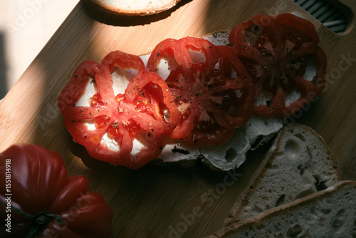 A rustic flat lay featuring slices of homemade artisan bread, fresh heirloom tomato, peppers on a wooden kitchen table. Natural light and cozy farmhouse aesthetics