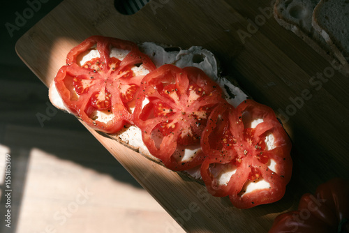 A rustic flat lay featuring slices of homemade artisan bread, fresh heirloom tomato, peppers on a wooden kitchen table. Natural light and cozy farmhouse aesthetics