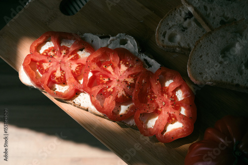 A rustic flat lay featuring slices of homemade artisan bread, fresh heirloom tomato, peppers on a wooden kitchen table. Natural light and cozy farmhouse aesthetics
