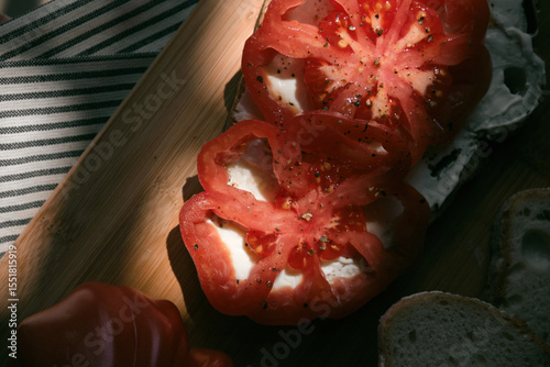 A rustic flat lay featuring slices of homemade artisan bread, fresh heirloom tomato, peppers on a wooden kitchen table. Natural light and cozy farmhouse aesthetics