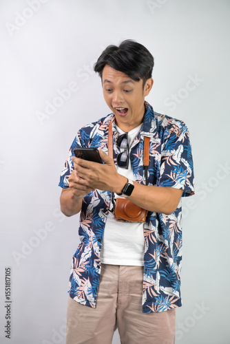 Happy young asian man wearing blue summer shirt is holding a smartphone with blank screen for mock up mockup, isolated over white background.