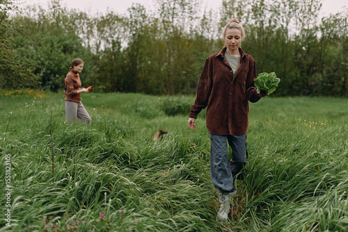 Middle age woman holding fresh greens in nature, enjoying active lifestyle, health, wellness, and wellbeing outdoors in lush green field under soft daylight.
