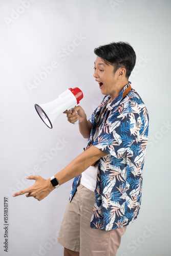 Handsome young asian man wearing blue summer shirt is shouting using a megaphone, isolated over white background.