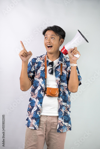 Handsome young asian man wearing blue summer shirt is shouting using a megaphone, isolated over white background.