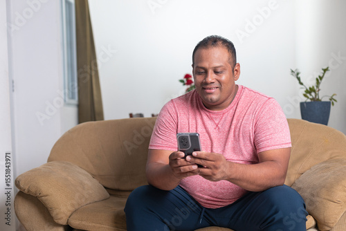 A man is sitting on a couch and looking at his cell phone