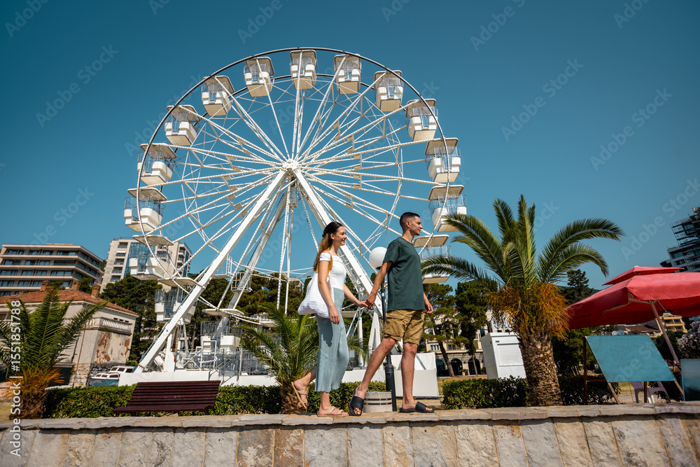 Fototapeta premium Couple Holding Hands Walking by the Ferris Wheel on a Summer Day
