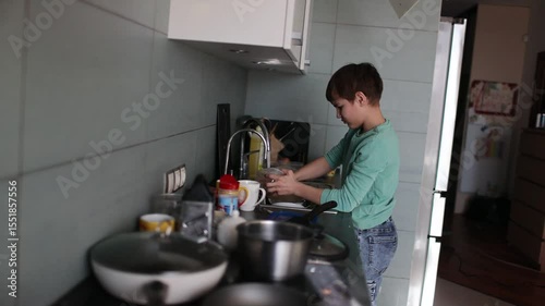 preteen boy washes dishes at home in the kitchen. helping parents. Domestic duties