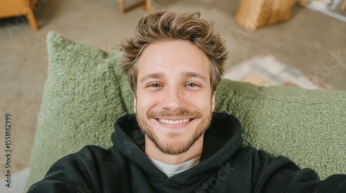A happy man is seen lying in bed from an overhead perspective, his head resting on a matching pillow with his eyes closed and a warm smile on his face