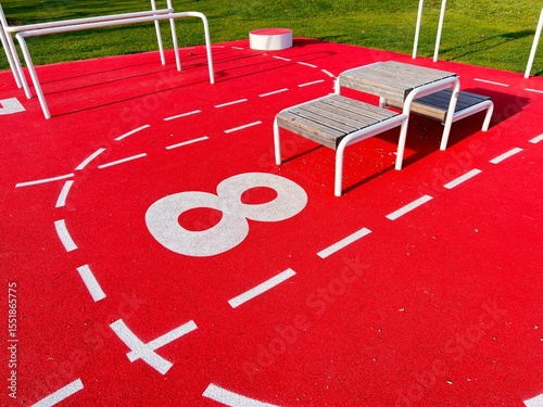 A station numbered eight on a red fitness trail. The red floor with white markings is elastic.