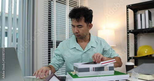 an architect is working in his office, a chief architect is reviewing the design plans before construction begins, an architect brings in blueprints and a model of a house to check for accuracy