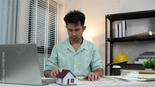 an architect is working in his office, a chief architect is reviewing the design plans before construction begins, an architect brings in blueprints and a model of a house to check for accuracy