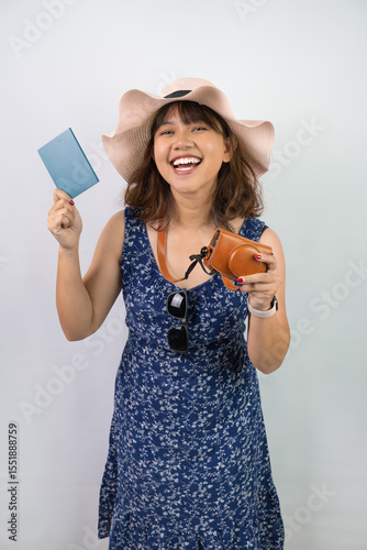 Beautiful young asian woman wearing blue summer dress and beach straw hat is holding indonesian passport, isolated over white background.
