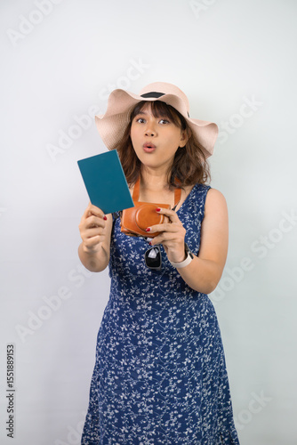 Beautiful young asian woman wearing blue summer dress and beach straw hat is holding indonesian passport, isolated over white background.