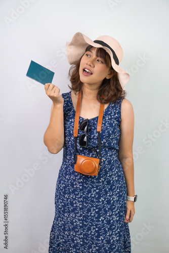 Beautiful young asian woman wearing blue summer dress and beach straw hat is holding indonesian passport, isolated over white background.