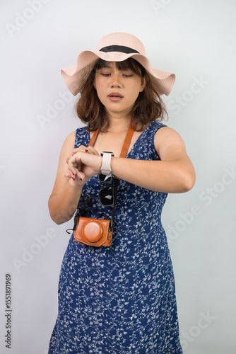Shocked young asian tourist woman wearing blue summer dress and hat is staring her smartwatch screen because the time has already passed or late, isolated over white background. Miss a flight