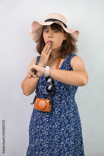 Shocked young asian tourist woman wearing blue summer dress and hat is staring her smartwatch screen because the time has already passed or late, isolated over white background. Miss a flight