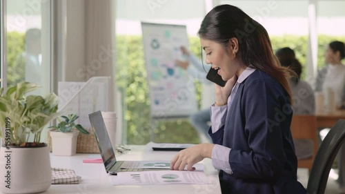 Real estate agent female asia people go green net zero waste control ESG audit office desk. Young adult woman asian SDGs auditor busy happy work using mobile phone call advice stock trader specialist.