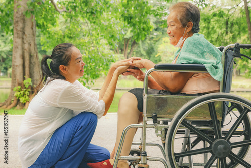 Fotografie Daughter caring an elderly disabled woman who has had her legs amputated and is in a wheelchair and is being treated diabetes holds prosthetic leg to be fitted relieve her disability