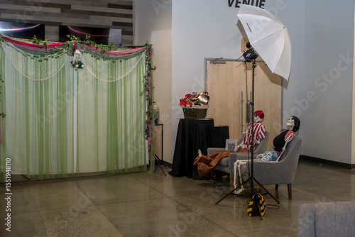  A whimsical photo booth setup features two pirate-costumed skeletons seated in chairs, complete with props and a lighting umbrella. The decorated backdrop suggests a festive or themed event.