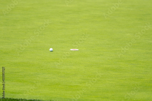 A golf ball rests near the edge of the hole on a perfectly manicured putting green. The vibrant green expanse emphasizes the precision required in golf.