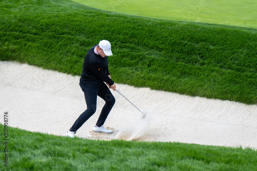 A golfer executes a powerful bunker shot, sending sand and the golf ball flying. This dynamic image captures the challenge and action of playing from a sand trap on a golf course.