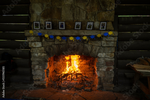 A large stone fireplace with a roaring fire dominates a rustic log cabin interior. Benches flank the hearth, creating a cozy and inviting atmosphere.