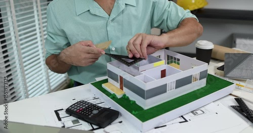 an architect is working in his office, a chief architect is reviewing the design plans before construction begins, an architect brings in blueprints and a model of a house to check for accuracy
