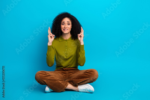 Photography Young woman seated casually on a blue background crossing fingers in hope wearin