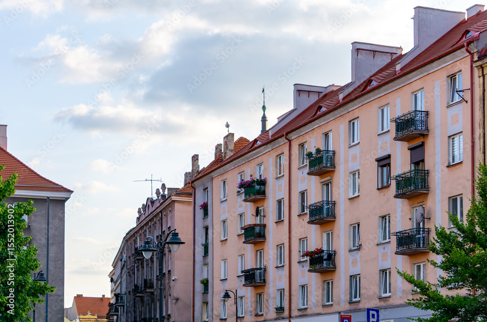 Fototapeta premium Row of residential buildings with red gable roofs and balconies decorated with flowers. Classic post-war urban architecture under a partly cloudy sky.