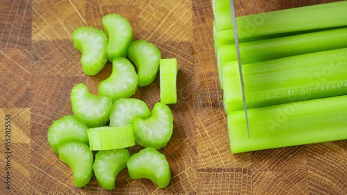 Food preparation. Chef with kitchen knife slices celery stalks on wooden board.