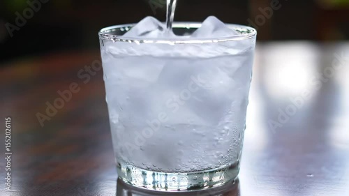 Macro Shot of Sparkling Soda Pouring Over Ice in Clear Glass with Bubbles and Condensation