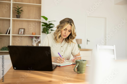 A woman in a casual setting writes notes while seated at a dining table, blending leisure and productivity beautifully.