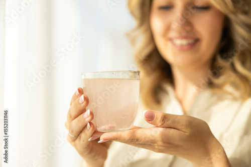 A woman holds a glass of water with an effervescent tablet in it. Healthy living, taking supplements, vitamins and minerals